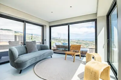 a living room with a couch and chairs and large windows at House of Cork and Ivy - By WeHost in Câmara de Lobos