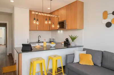 a living room with a couch and a kitchen with yellow stools at Alegria Flat by An Island Apart in Funchal
