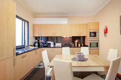 a kitchen with a wooden table and white chairs at Moradia Casa Feliz in Santa Cruz