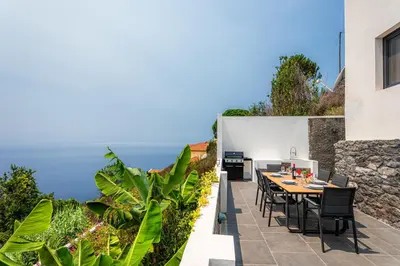 a patio with a table and chairs and the ocean at Meerblick - 3-Bett Villa mit Terrassen & Hot-Tub in Fajã da Ovelha