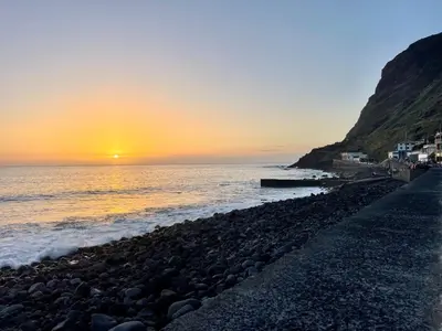 a beach with the sun setting on the water at Blue by the Sea House in Paul do Mar