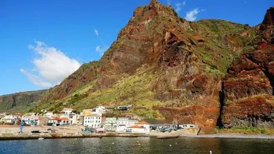 a mountain next to a body of water with houses at Blue by the Sea House in Paul do Mar