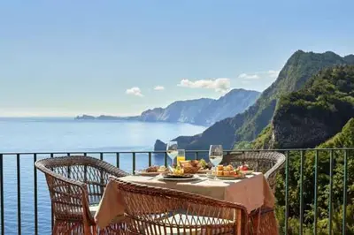 a table with food and wine glasses on a balcony at Blue by the Sea House in Paul do Mar