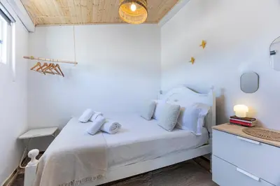 a white bedroom with a white bed with blue pillows at Casa Ana Mar in Vila do Bispo