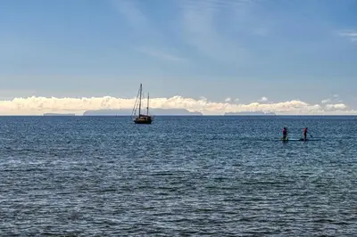 two people standing on a paddle board in the water with a boat at Baia Machico, a Home in Madeira in Machico