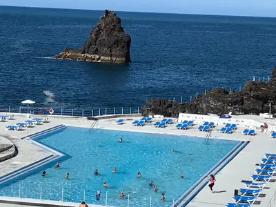 a large swimming pool with people in the ocean at Apartamentos do Mar Funchal in Funchal