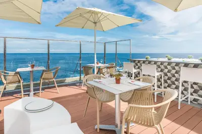 a patio with tables and chairs and the ocean at Studios by Aqua Natura Hotels in Porto Moniz