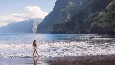 a woman walking on the beach near the water at Studios by Aqua Natura Hotels in Porto Moniz