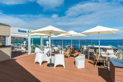 a deck with white chairs and tables and umbrellas at Studios by Aqua Natura Hotels in Porto Moniz