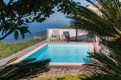 a swimming pool with two chairs and the ocean in the background at OurMadeira - Casa Florenças in Calheta