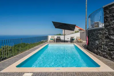 a swimming pool with an umbrella next to a building at OurMadeira - Casa Florenças in Calheta