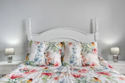 a white bedroom with a bed with a floral bedspread at Casa da Ribeira da Janela in Porto Moniz