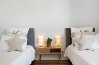 two beds with white pillows and a table with two lamps at Casa Castanheta in Câmara de Lobos