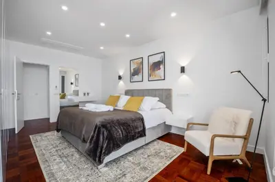 a white bedroom with a bed and a chair at Lido Sunrise Apartment by Homie in Funchal