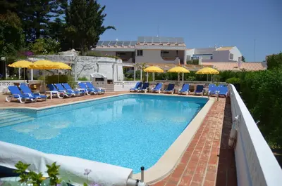 a swimming pool with blue chairs and umbrellas at Garden T2 Apartment in Luz in Luz