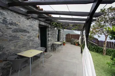 a patio with tables and chairs under a wooden pergola at Cozy and traditional stone house in Arco da Calheta