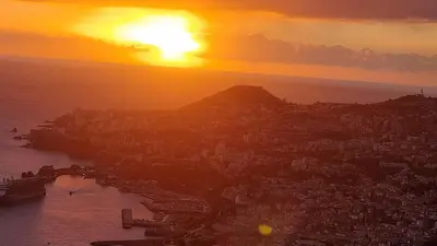a view of a city with the sun setting over the ocean at Villa das Furnas in Funchal
