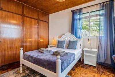 a bedroom with a bed with blue curtains and a window at De Freitas Home by Rent-a-key in Porto Moniz
