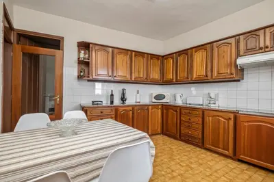 a kitchen with wooden cabinets and a table with white chairs at De Freitas Home by Rent-a-key in Porto Moniz