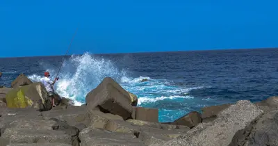 a man fishing on the rocks near the ocean at Rita's house in Ponta Delgada