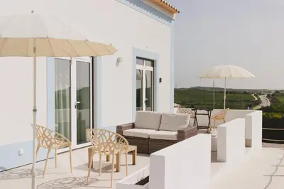 a patio with chairs and a couch and an umbrella at Pure Flor de Esteva in Vila do Bispo