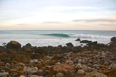 a rocky beach with a wave in the ocean at Pure Flor de Esteva in Vila do Bispo