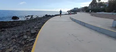 a person walking along a sidewalk next to the water at Reis Magos Beach Caniço Sea line Apartment in Caniço