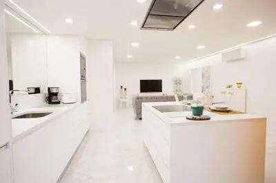 a kitchen with white cabinets and a living room at Pérola dos Anjos by LovelyStay in Funchal