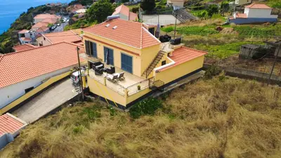 a yellow house with an orange roof on a hill at Casa Gomes in Calheta