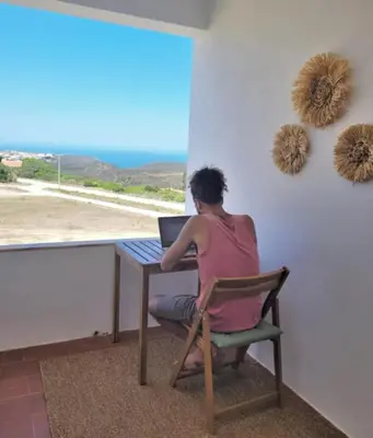 a woman sitting at a table with a laptop at Arrifana Sunset & Ocean View in Aljezur
