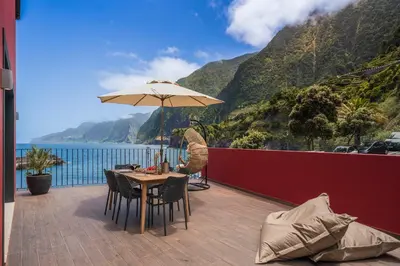 a table with an umbrella on a balcony with a view of the ocean at Pipas do Avô - Seixal by An Island Apart in Porto Moniz