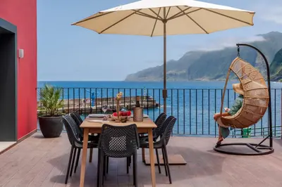 a table and chairs with an umbrella on a balcony at Pipas do Avô - Seixal by An Island Apart in Porto Moniz