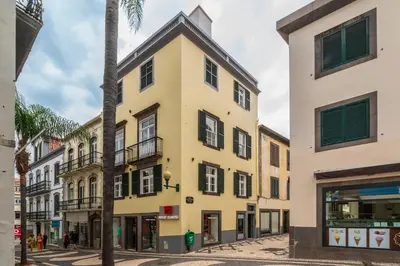 a yellow building on a street with a palm tree at Queimada Lodges by An Island Apart in Funchal