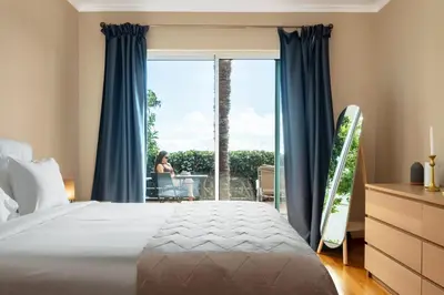 a bedroom with a bed and a window with a woman sitting at a table at Magnolia Sunsets in Calheta