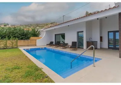 a white house with a balcony and a yard at The pool house in Ponta de Sol in Funchal