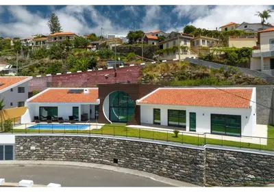 a house with a stone wall next to a city at The pool house in Ponta de Sol in Funchal