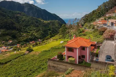 a pink house with an orange roof on a hill at Casa do Rosário by An Island Apart in São Vicente
