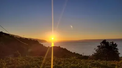 a sunset over the ocean with the sun setting on a hill at Faria's House in Ponta Delgada
