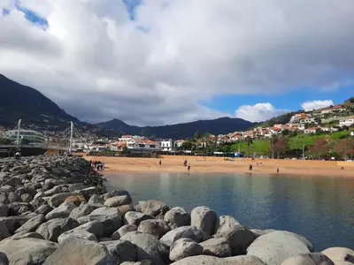 a beach with a bunch of rocks in the water at Sunny Beach Machico Apartment by Holiday Rental Madeira in Machico