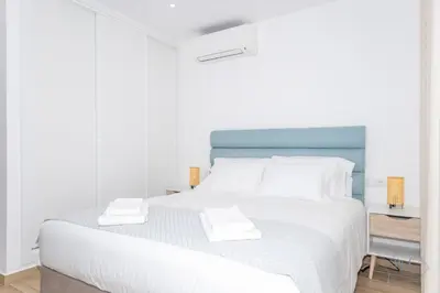 a white bedroom with a large bed with a blue headboard at MC Suites Burgau with amazing front sea view in Burgau