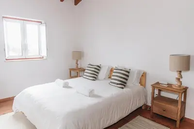 a bedroom with a white bed with pillows and a window at Casa Nook Arrifana in Aljezur