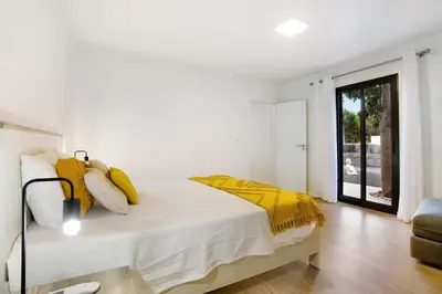 a white bedroom with a bed with yellow pillows at Casa Fonte São João in Vila Baleira