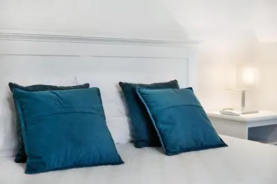 a white bed with blue pillows and a white headboard at Casa Fonte São João in Vila Baleira