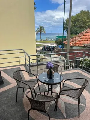 a table with chairs and a vase of flowers on a balcony at Vivenda da Praia in Machico