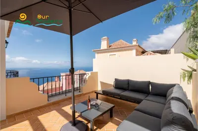 a patio with a couch and an umbrella on a balcony at OurMadeira - Palheiro Eagle in Funchal