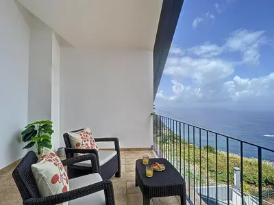 a balcony with two chairs and a table and the ocean at Vinhaticos Villa by Atlantic Holiday in Porto Moniz