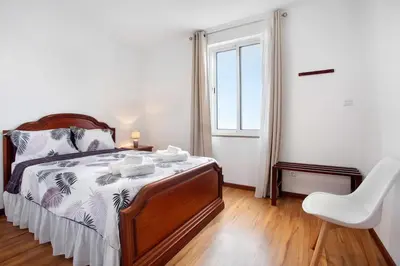 a bedroom with a bed with a chair and a window at Simão House in Calheta