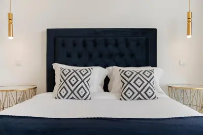 a bed with a black headboard and two tables at The White House by An Island Apart in Ponta do Sol