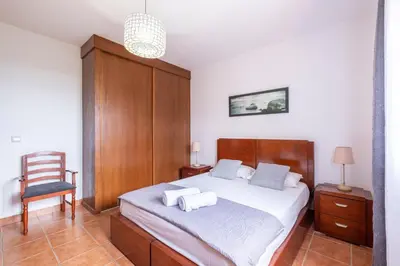 a bedroom with a bed with a wooden headboard and a chair at Casa del Mar I by GALMI in Arco de São Jorge