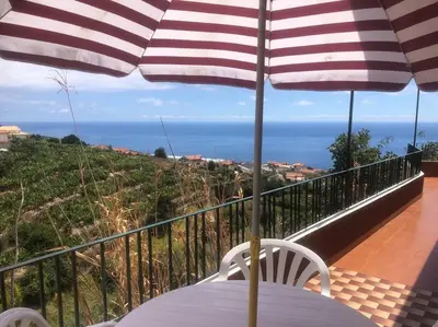 a table with an umbrella on a balcony with the ocean at Casa Vista Mar -2 bedrooms,fantastic Seaview in Estreito da Calheta